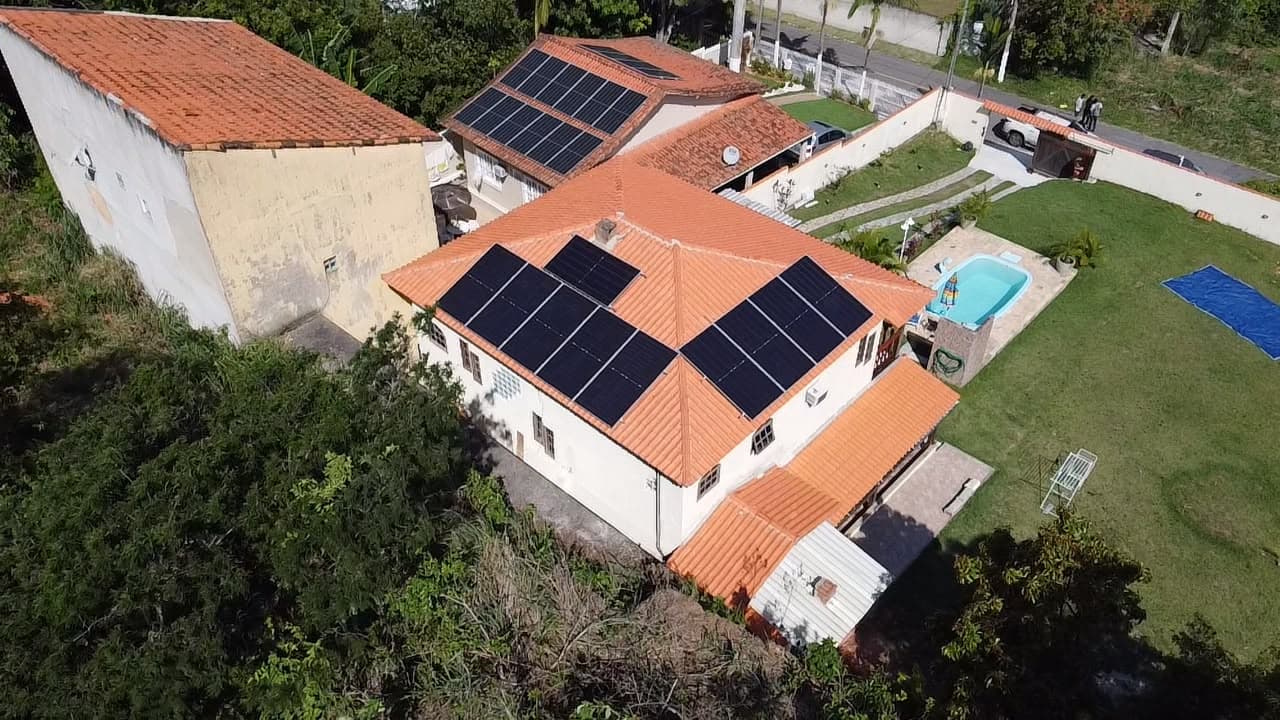 Vista aérea de casa com telhado de telhas laranja, piscina e painéis solares instalados em duas águas do telhado